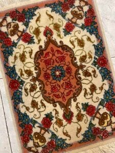 Azerbaijan Tappeti Milano Piccolo tappeto ornato con motivi floreali rossi, blu e crema e un medaglione centrale, adagiato su un pavimento piastrellato.