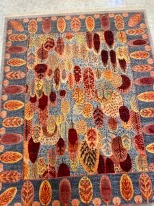 Azerbaijan Tappeti Milano Un tappeto colorato con vari motivi di foglie autunnali nei toni del rosso, dell'arancio, del giallo e del marrone su uno sfondo grigio.