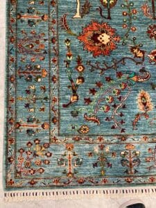 Azerbaijan Tappeti Milano Angolo di un tappeto blu a motivi floreali con disegni intricati e frange bianche sul bordo.