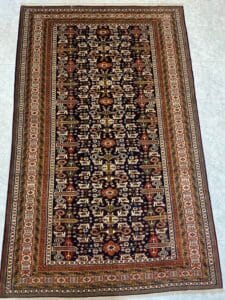 Azerbaijan Tappeti Milano Tappeto persiano rettangolare con intricati motivi geometrici e floreali in colori scuri e terrosi su un pavimento piastrellato chiaro.