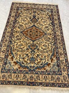 Azerbaijan Tappeti Milano Tappeto a motivi beige e blu con intricati disegni floreali e un medaglione centrale, esposto su un pavimento piastrellato.