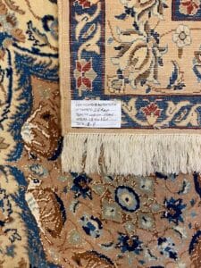 Azerbaijan Tappeti Milano Angolo di un tappeto a fantasia con etichetta del certificato e bordo sfrangiato visibile su sfondo blu e beige.