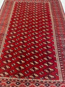 Azerbaijan Tappeti Milano Tappeto a motivi rossi con disegni geometrici e un logo a forma di foglia colorata nell'angolo in alto a destra.