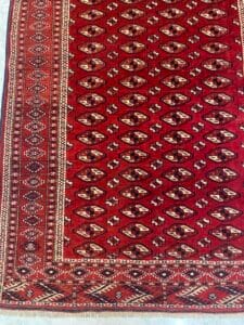 Azerbaijan Tappeti Milano Tappeto a motivi rossi con disegni geometrici e una girandola colorata nell'angolo in alto a destra.