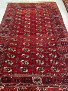 Azerbaijan Tappeti Milano Tappeto a fantasia rossa con intricati disegni geometrici, bordi bordati e un logo a forma di farfalla colorata nell'angolo.