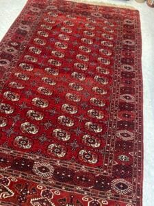 Azerbaijan Tappeti Milano Un tappeto rosso con disegni geometrici intricati su un pavimento piastrellato chiaro.