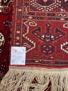 Azerbaijan Tappeti Milano Primo piano di un tappeto a fantasia rossa con frange bianche e una piccola etichetta bianca nell'angolo.