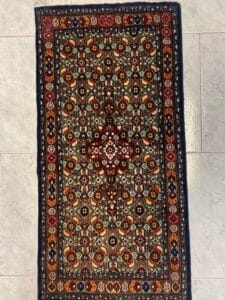 Azerbaijan Tappeti Milano Tappeto rettangolare in stile persiano con intricati motivi floreali in rosso, blu e oro su un pavimento piastrellato.