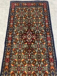 Azerbaijan Tappeti Milano Un tappeto a motivi colorati con intricati disegni floreali e un medaglione centrale su un pavimento piastrellato.