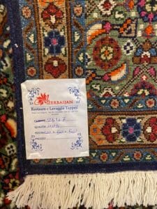 Azerbaijan Tappeti Milano Primo piano di un tappeto a motivi colorati con un'etichetta scritta in italiano e azero attaccata all'angolo.