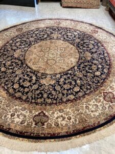 Azerbaijan Tappeti Milano Tappeto rotondo in stile persiano con intricati motivi floreali nei toni del blu, crema e rosso, caratterizzato da un medaglione centrale decorato e bordi con frange su un pavimento piastrellato.