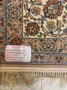 Azerbaijan Tappeti Milano Tappeto persiano dettagliato con motivo floreale e bordo sfrangiato. Un'etichetta scritta a mano in italiano fornisce informazioni su numero, origine, qualità, composizione e dimensioni del tappeto. Il tappeto è posato su un pavimento piastrellato.