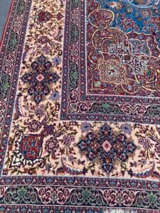 Azerbaijan Tappeti Milano Tappeto ornato in stile persiano con intricati motivi floreali e geometrici nei toni del rosso, blu e crema. Un colorato disegno astratto sovrasta un angolo.