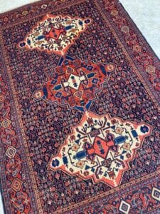 Azerbaijan Tappeti Milano Tappeto tradizionale in stile persiano con intricati motivi geometrici e floreali nei toni del rosso, del blu, del bianco e del nero, caratterizzato da tre grandi medaglioni a diamante al centro e da un logo a farfalla multicolore nell'angolo in alto a destra.