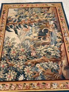 Azerbaijan Tappeti Milano Tappeto rettangolare con un dettagliato bordo floreale e una scena di natura con uccelli, alberi e fiori nei toni del blu, del verde e del marrone. Una farfalla colorata si trova nell'angolo in alto a destra.