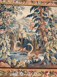 Azerbaijan Tappeti Milano Un arazzo dettagliato raffigura due anatre che nuotano in uno stagno circondato da un fogliame rigoglioso, fiori e alberi, con colline e un edificio a cupola sullo sfondo lontano.