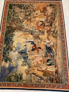 Azerbaijan Tappeti Milano Un arazzo dettagliato e decorato raffigura un grande gruppo di persone in abiti storici, riunite all'aperto tra alberi e montagne, con un bordo decorativo caratterizzato da motivi intricati.