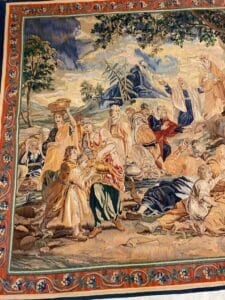 Azerbaijan Tappeti Milano Un arazzo dettagliato e colorato raffigura una scena storica o biblica con molte persone in abiti fluenti, alcune in piedi e altre in ginocchio, ambientata all'aperto con alberi, nuvole e montagne sullo sfondo. Un bordo ornato circonda la scena.