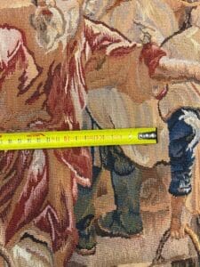 Azerbaijan Tappeti Milano Un nastro di misurazione giallo è teso su un arazzo con una scena colorata che mostra persone in abiti d'epoca. Il nastro misura circa 22 cm. Nell'angolo in alto a destra è presente un logo multicolore con una farfalla e la lettera "A".