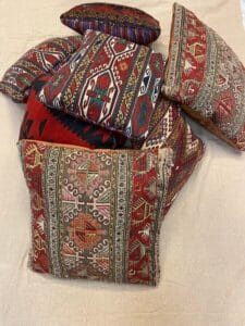 Azerbaijan Tappeti Milano Diversi cuscini con motivi tradizionali e disegni geometrici intricati e colorati sono disposti su uno sfondo di tessuto chiaro. Un cuscino presenta una piccola decorazione a forma di foglia multicolore.