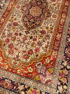 Azerbaijan Tappeti Milano Tappeto ornato in stile persiano con intricati motivi floreali in rosso, crema, rosa, verde e blu. Nella parte superiore destra dell'immagine compare una farfalla colorata che contrasta con il disegno tradizionale.