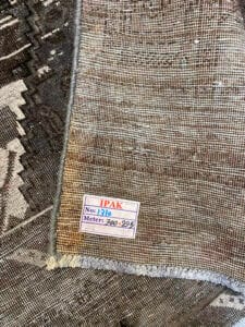 Azerbaijan Tappeti Milano Primo piano di un tessuto intrecciato con un'etichetta che riporta la scritta "IPAK" e le misure "Metri: 300-295". Sopra il tessuto è presente un logo colorato.