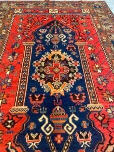 Azerbaijan Tappeti Milano Un tappeto persiano colorato con intricati motivi geometrici e floreali nei toni del rosso, del blu e del crema. Il disegno centrale presenta un medaglione simmetrico e motivi stilizzati delimitati da bordi dettagliati.