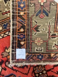 Azerbaijan Tappeti Milano Primo piano di due tappeti a motivi sovrapposti, con un angolo ribaltato per mostrare la parte inferiore. Un foglietto con la scritta "2622 150x115" è appoggiato sul tappeto e nell'angolo in alto a destra compare un logo colorato a forma di foglia.