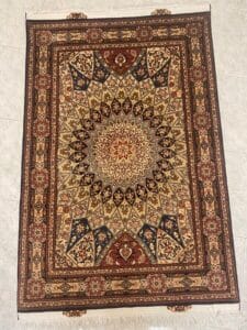 Azerbaijan Tappeti Milano Tappeto persiano rettangolare con intricati motivi geometrici e floreali nei toni del marrone, beige, blu e rosso, esposto su un pavimento piastrellato chiaro. Nell'angolo in alto a destra è presente il logo di una farfalla colorata.