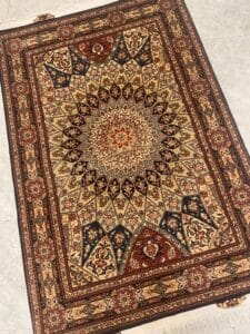 Azerbaijan Tappeti Milano Tappeto persiano dalla ricca fantasia con un disegno centrale a medaglione a stella nei toni del beige, marrone, rosso e verde scuro. I bordi intricati incorniciano motivi floreali e geometrici simmetrici. Il tappeto è posato su un pavimento piastrellato chiaro.