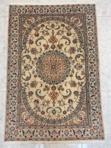 Azerbaijan Tappeti Milano Tappeto rettangolare in stile persiano con sfondo beige, intricati motivi floreali e un medaglione centrale dettagliato nei toni del marrone, del blu e del crema, delimitato da un disegno floreale blu e beige; nell'angolo è presente un logo colorato.