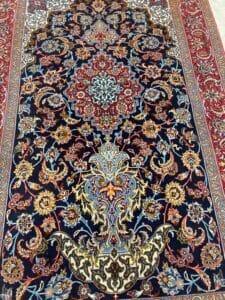Azerbaijan Tappeti Milano Tappeto persiano dalla ricca fantasia con intricati disegni floreali e di viti nei toni del blu, rosso, crema e oro. Il tappeto presenta un medaglione centrale e bordi ornati, con un logo a farfalla multicolore nell'angolo.
