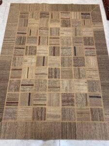 Azerbaijan Tappeti Milano Un tappeto patchwork beige e marrone con motivi quadrati su un pavimento piastrellato, con un logo colorato nell'angolo in alto a destra.