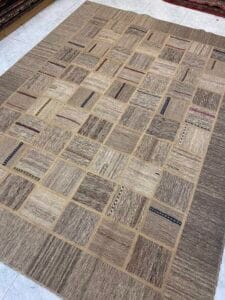 Azerbaijan Tappeti Milano Un grande tappeto patchwork beige e marrone con vari motivi quadrati disposto su un pavimento piastrellato.