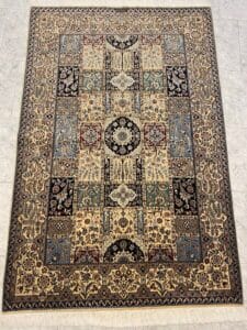 Azerbaijan Tappeti Milano Tappeto rettangolare in stile persiano con intricati motivi floreali e geometrici nei toni del beige, blu, verde, rosso e nero. Il tappeto è posizionato su un pavimento piastrellato chiaro e nell'angolo in alto a destra è presente un logo colorato.