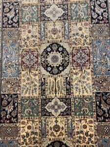 Azerbaijan Tappeti Milano Tappeto a fantasia con intricati disegni floreali e geometrici nei colori crema, blu, verde e nero, diviso in sezioni rettangolari. Nell'angolo in alto a destra compare il logo di una farfalla colorata.