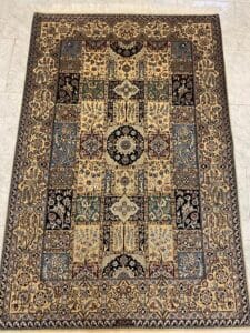 Azerbaijan Tappeti Milano Tappeto rettangolare in stile persiano con intricati motivi floreali e geometrici nei toni del beige, blu, verde e nero. Una farfalla colorata decora l'angolo superiore destro del tappeto. Il tappeto è posato su un pavimento piastrellato.