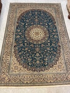 Azerbaijan Tappeti Milano Tappeto persiano ornato di forma ovale con intricati motivi floreali in oro e beige su uno sfondo verde scuro, delimitato da un'ampia sezione dettagliata in beige e oro, posato su un pavimento piastrellato chiaro.