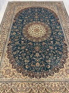 Azerbaijan Tappeti Milano Un grande tappeto ornato in stile persiano con un intricato medaglione centrale, motivi floreali color verde scuro e beige e un bordo decorativo. Un logo astratto multicolore si trova nell'angolo in alto a destra.