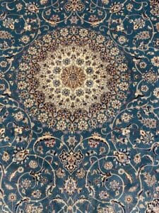 Azerbaijan Tappeti Milano Tappeto ornato in stile persiano con un dettagliato motivo floreale circolare al centro su uno sfondo verde acqua. In alto a destra è presente una grafica colorata e stilizzata a forma di uccello.