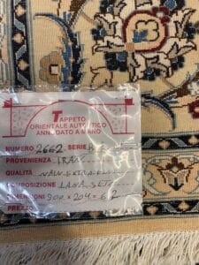 Azerbaijan Tappeti Milano Primo piano di un'etichetta su un tappeto orientale a motivi. L'etichetta riporta dettagli scritti a mano in italiano sul tappeto, tra cui l'origine (Iran), il materiale (lana e seta), le dimensioni e la qualità.