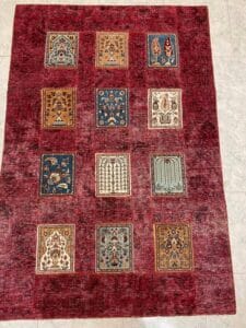 Azerbaijan Tappeti Milano Un tappeto rosso rettangolare con una griglia di dodici quadrati decorati nei toni del marrone, del blu e del grigio, con vari disegni intricati.