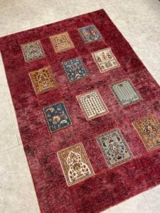 Azerbaijan Tappeti Milano Un tappeto a fantasia rossa con vari motivi rettangolari in blu, beige e bianco è adagiato su un pavimento piastrellato.