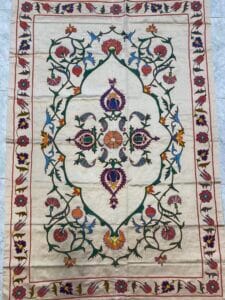 Azerbaijan Tappeti Milano Un arazzo colorato e decorato con intricati motivi floreali e un disegno centrale simmetrico su uno sfondo beige è adagiato su un pavimento piastrellato.