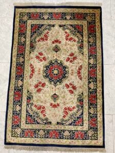 Azerbaijan Tappeti Milano Un tappeto rettangolare decorato con un motivo floreale nei colori rosso, blu e beige, caratterizzato da un medaglione centrale e bordi intricati.