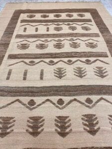 Azerbaijan Tappeti Milano Un tappeto intrecciato beige e marrone con motivi geometrici simmetrici e un logo a forma di foglia multicolore nell'angolo.