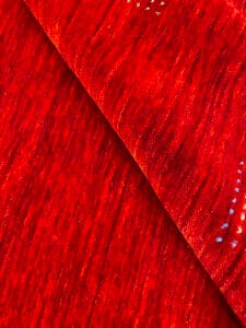 Azerbaijan Tappeti Milano Un primo piano di tessuto rosso con una texture visibile. L'angolo in alto a destra presenta un motivo di foglia ricamato colorato.