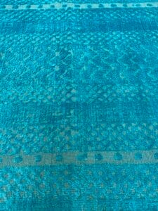 Azerbaijan Tappeti Milano Un tessuto con fantasia blu e un logo colorato raffigurante foglie stilizzate e una lettera "A" nell'angolo in alto a destra.