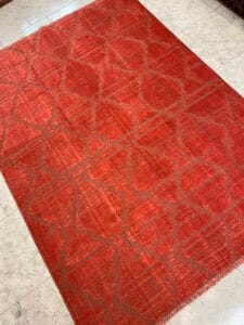 Azerbaijan Tappeti Milano Un tappeto rosso con motivi geometrici su un pavimento chiaro.