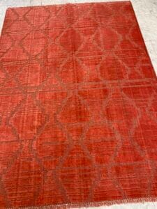 Azerbaijan Tappeti Milano Un tappeto rosso a fantasia su un pavimento piastrellato con un logo a forma di foglia colorata in un angolo.